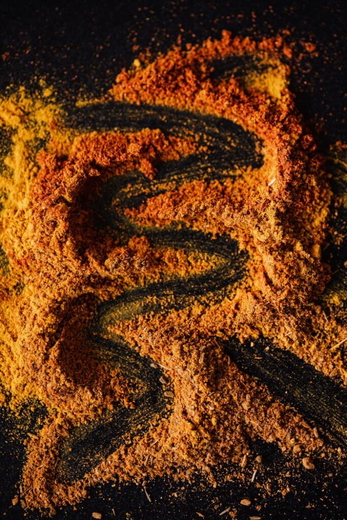 A creative top view of colorful spices scattered on a black background, showcasing a rich texture.